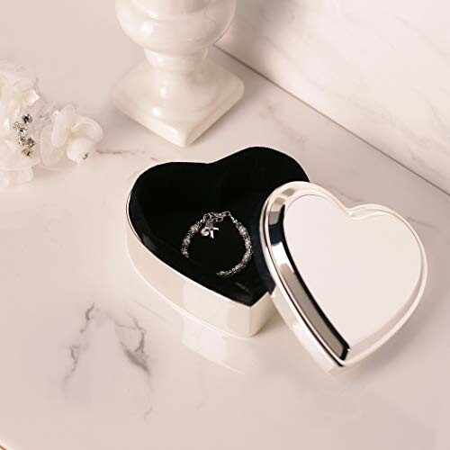 Heart-shaped silver jewelry box with a bracelet inside on a marble surface.